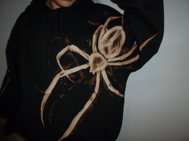 Black hoodie with a large beige spider bleach design on a plain background
