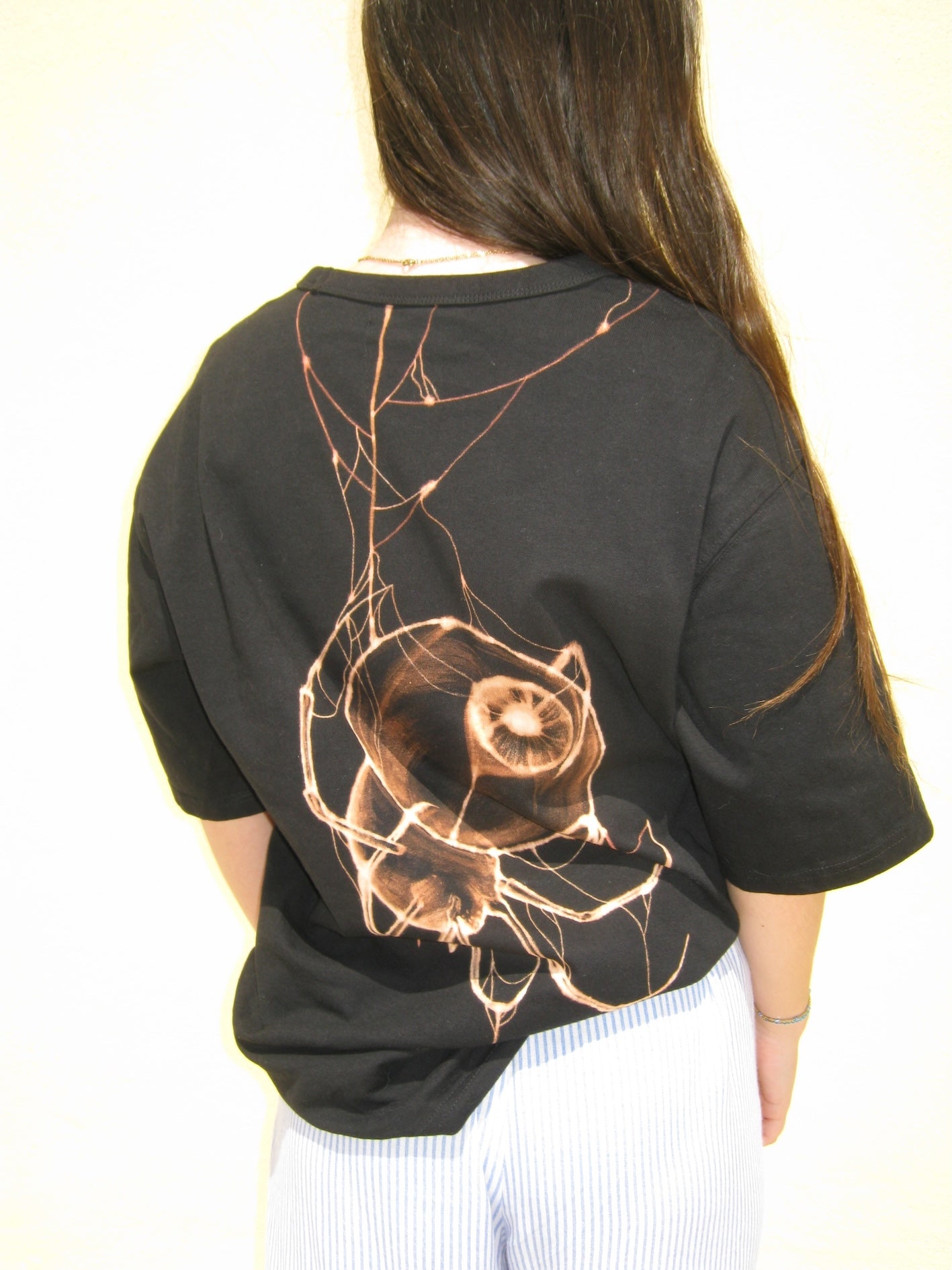 Person wearing a black t-shirt with a bleach spider design on the back against a white background. algarve