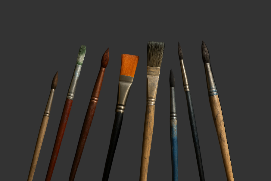 Set of paintbrushes with various bristle shapes and handles on a dark background
