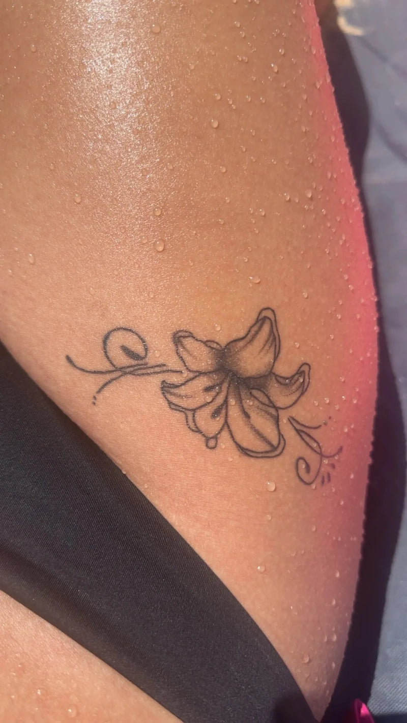 Tattoo of a flower on a person's leg with water droplets.