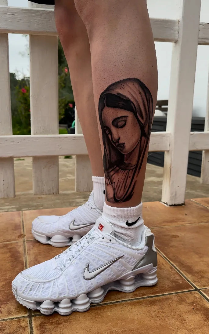 Person wearing white Nike sneakers with a detailed tattoo on their leg.