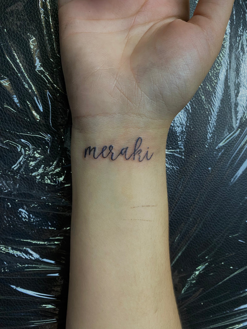 Hand with a tattoo of 'meraki' in cursive, Almancil.
