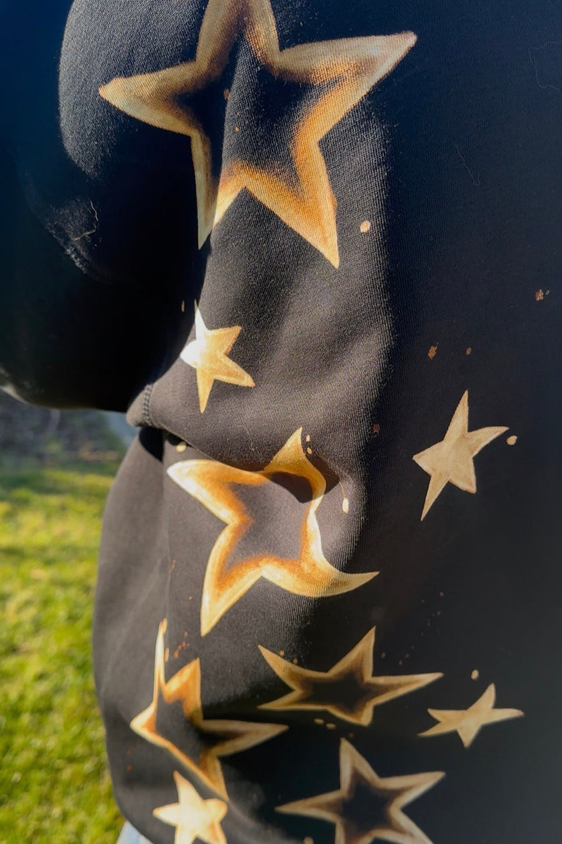 Black hoodie with bleach star patterns worn outdoors on a grassy area