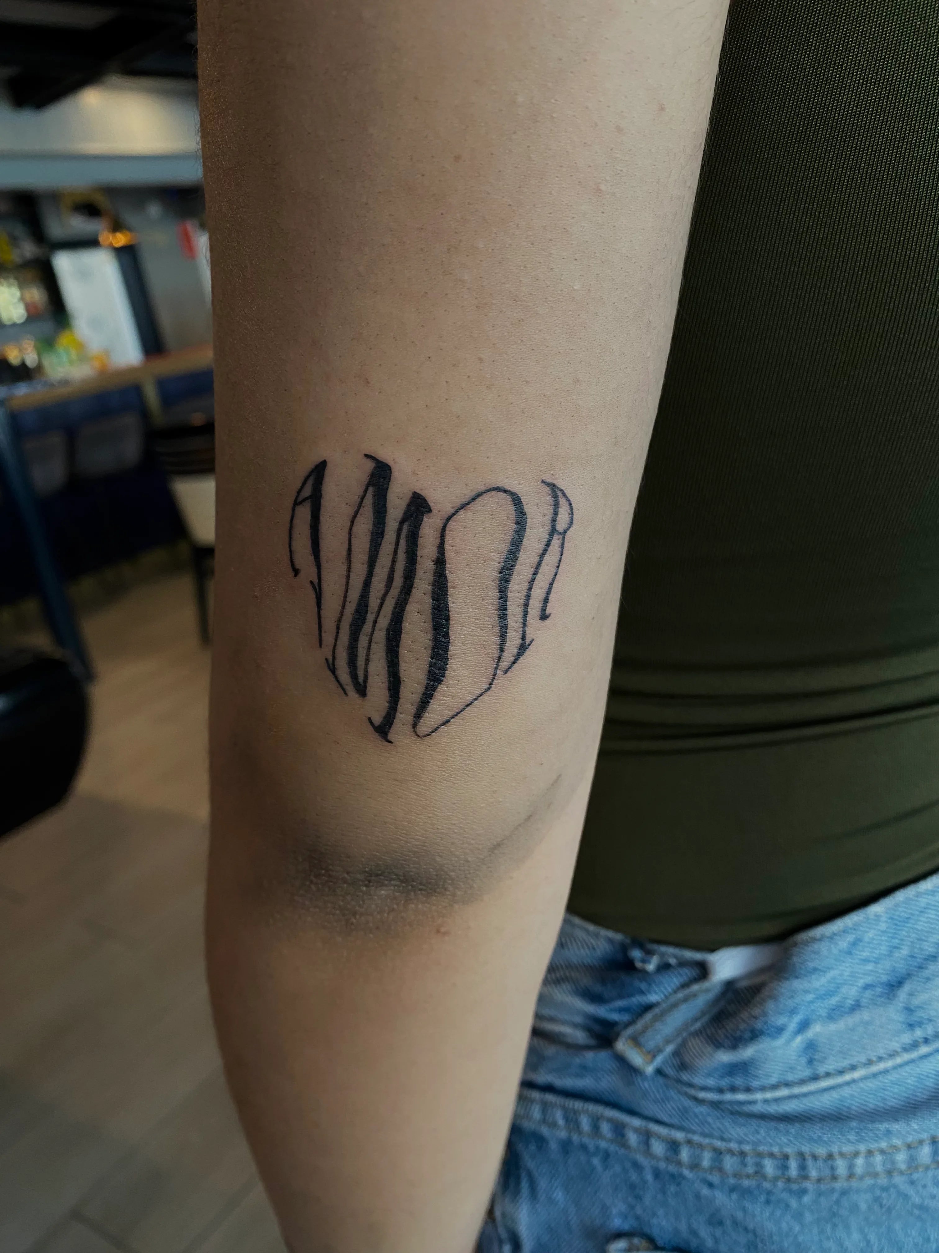 Tattoo of the word 'AMOR' on a person's arm with a blurred background.